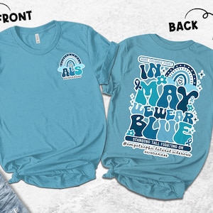 May include: A light blue t-shirt with the text "FRONT" and "BACK" above the shirt. The front of the shirt has a rainbow and the text "ALS awareness". The back of the shirt has the text "In May We Wear Blue" and "Standing Tall Fighting On".