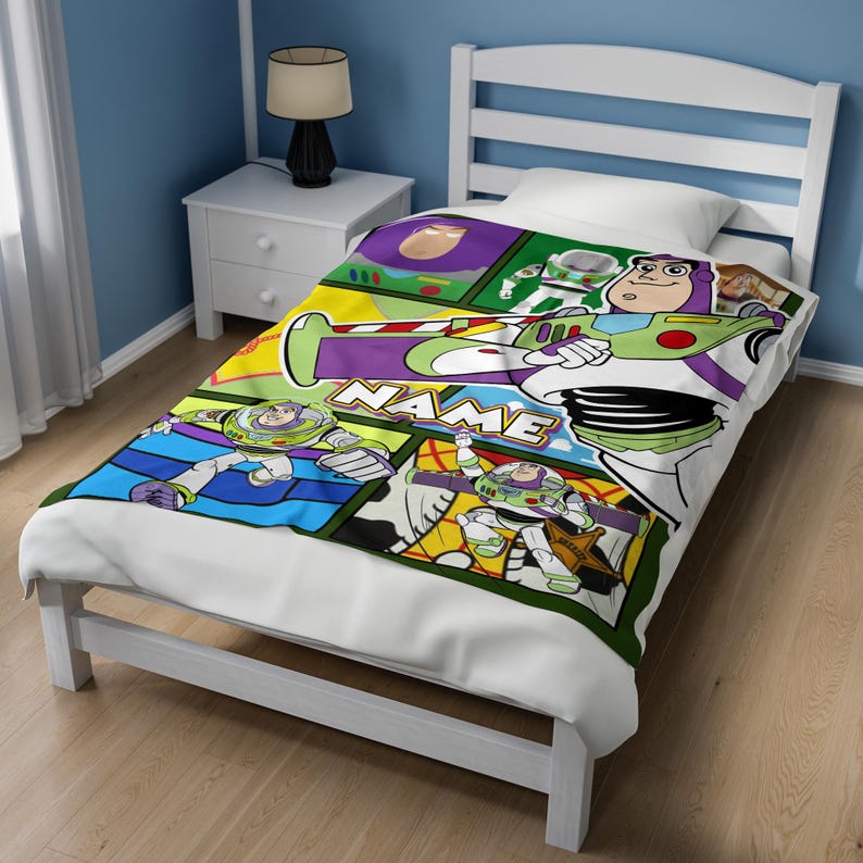 Puede incluir: Una manta de cama blanca con un estampado colorido estilo c&oacute;mic del personaje Buzz Lightyear en varias poses de acci&oacute;n. El dise&ntilde;o incluye paneles verdes, morados y azules con la palabra NAME impresa en letras blancas llamativas en el centro.