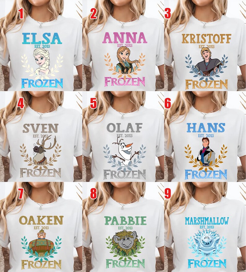 Puede incluir: Camisetas blancas con personajes de la pel&iacute;cula "Frozen". Cada camiseta tiene el nombre de un personaje, el texto "EST. 2013" y la palabra "FROZEN" en una fuente decorativa. Los personajes incluyen a Elsa, Anna, Kristoff, Sven, Olaf, Hans, Oaken, Pabbie y Marshmallow.