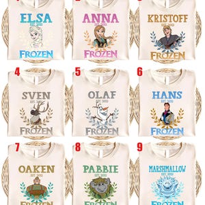 Puede incluir: Nueve camisetas color crema con personajes de la pel&iacute;cula "Frozen." Cada camiseta tiene el nombre de un personaje, el texto "EST. 2013" y la palabra "FROZEN." Los personajes incluyen Elsa, Anna, Kristoff, Sven, Olaf, Hans, Oaken, Pabbie y Marshmallow.