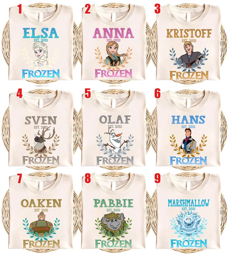 Puede incluir: Nueve camisetas color crema con personajes de la pel&iacute;cula "Frozen." Cada camiseta tiene el nombre de un personaje, el texto "EST. 2013" y la palabra "FROZEN." Los personajes incluyen Elsa, Anna, Kristoff, Sven, Olaf, Hans, Oaken, Pabbie y Marshmallow.