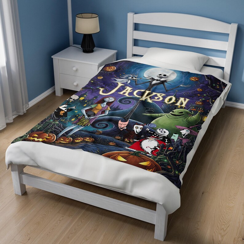 K&ouml;nnte beinhalten: Eine rechteckige Decke mit einem farbenfrohen Grafikdruck von Charakteren aus Nightmare Before Christmas, darunter Jack Skellington, Sally und Oogie Boogie, mit dem Namen JACKSON in gro&szlig;en gelben Buchstaben in der Mitte gedruckt.