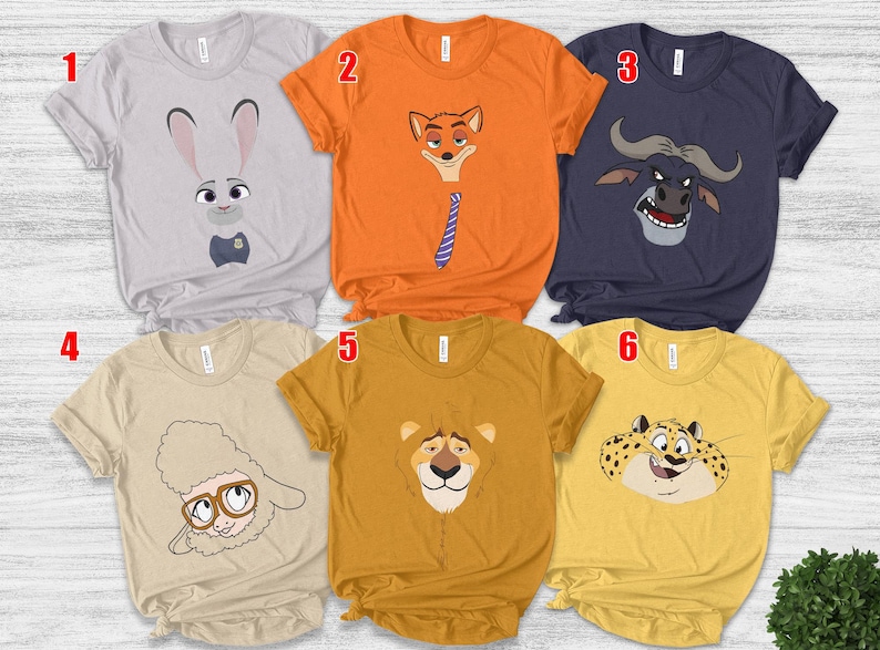 May include: Six short-sleeved t-shirts with cartoon animal faces. The shirts are light gray, orange, navy blue, tan, mustard yellow, and gold. The animal faces include a rabbit, fox, buffalo, sheep, lion, and leopard.