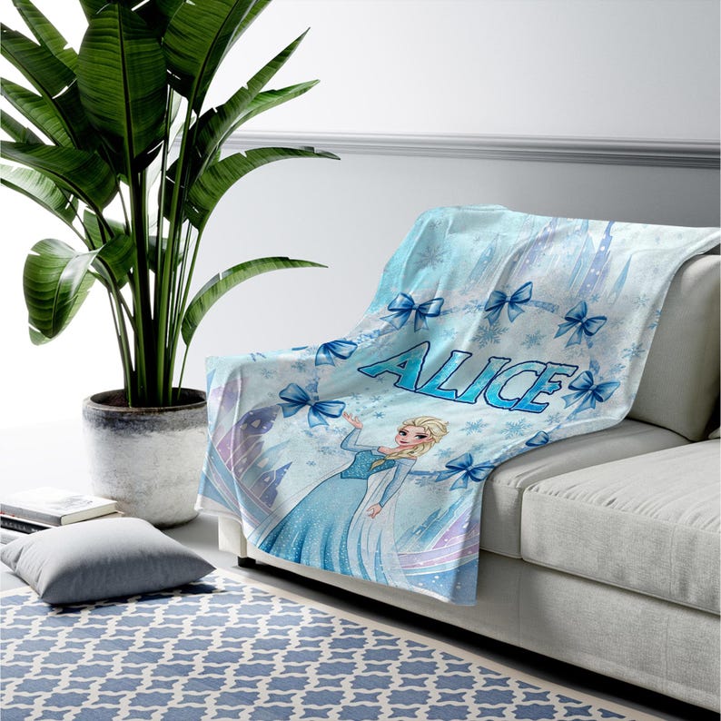 May include: A light blue throw blanket featuring a cartoon character with blonde hair in a blue gown, surrounded by blue bows and snowflake patterns. The name ALICE is printed in large blue letters across the center of the soft fabric.