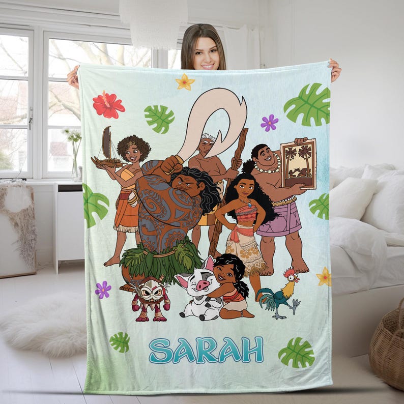 K&ouml;nnte beinhalten: Eine hellblaue Fleecedecke mit einem farbenfrohen Grafikdruck der Vaiana-Figuren, darunter Maui, Vaiana, Pua, Heihei und Kakamora. Das Design zeigt tropische Bl&auml;tter und Blumen sowie den Namen SARAH in gro&szlig;en blauen Buchstaben am unteren Rand.