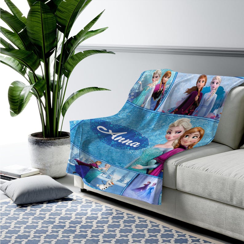May include: A soft throw blanket featuring a blue-toned collage of characters from the movie Frozen, including Elsa, Anna, and Olaf. The design includes multiple panels with the characters and the name Anna written in a white script font across the center.