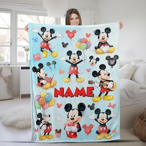 May include: A light blue fleece blanket featuring multiple illustrations of Mickey Mouse in various poses, including holding balloons, playing a guitar, and reading a book. The word NAME is printed in large red block letters in the center.