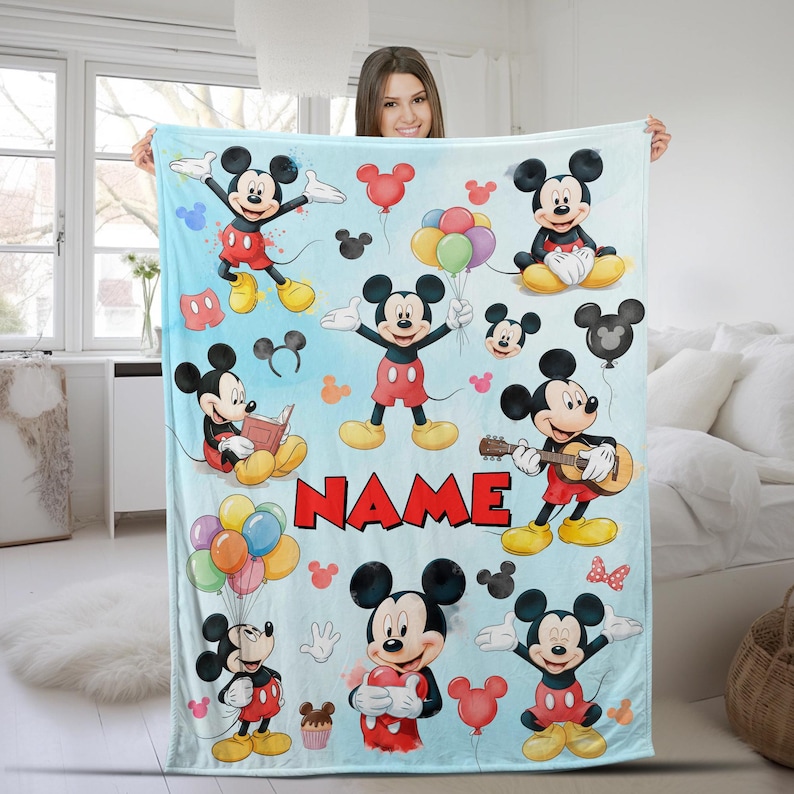 May include: A light blue fleece blanket featuring multiple illustrations of Mickey Mouse in various poses, including holding balloons, playing a guitar, and reading a book. The word NAME is printed in large red block letters in the center.