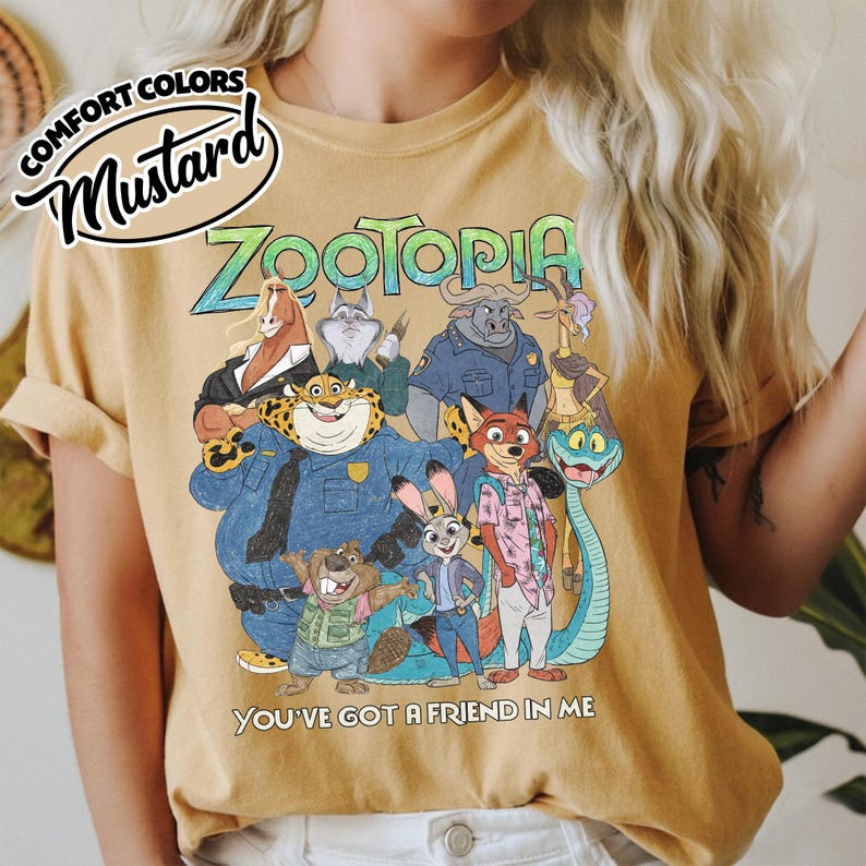 May include: Mustard-colored t-shirt featuring the word "Zootopia" in a colorful font, with a graphic of characters from the animated movie. The text "You've Got a Friend in Me" is below the graphic. The shirt has rolled-up sleeves.