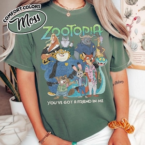 May include: Moss green t-shirt featuring the word "Zootopia" in blue and green, with a graphic of characters from the animated movie. The text "You've got a friend in me" is printed below the graphic.