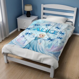 May include: A light blue fleece blanket featuring a cartoon character with blonde hair in a blue gown, surrounded by blue bows, snowflakes, and castle silhouettes. The name ALICE is printed in large blue letters across the center of the blanket.