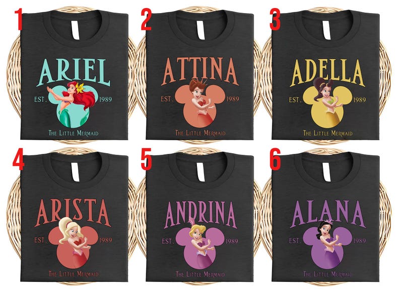 Puede incluir: Camisetas negras con nombres de "La Sirenita". Cada camiseta muestra un nombre, una ilustraci&oacute;n de personaje dentro de una cabeza de Mickey Mouse y el texto "EST. 1989". Los nombres incluyen Ariel, Attina, Adella, Arista, Andrina y Alana.