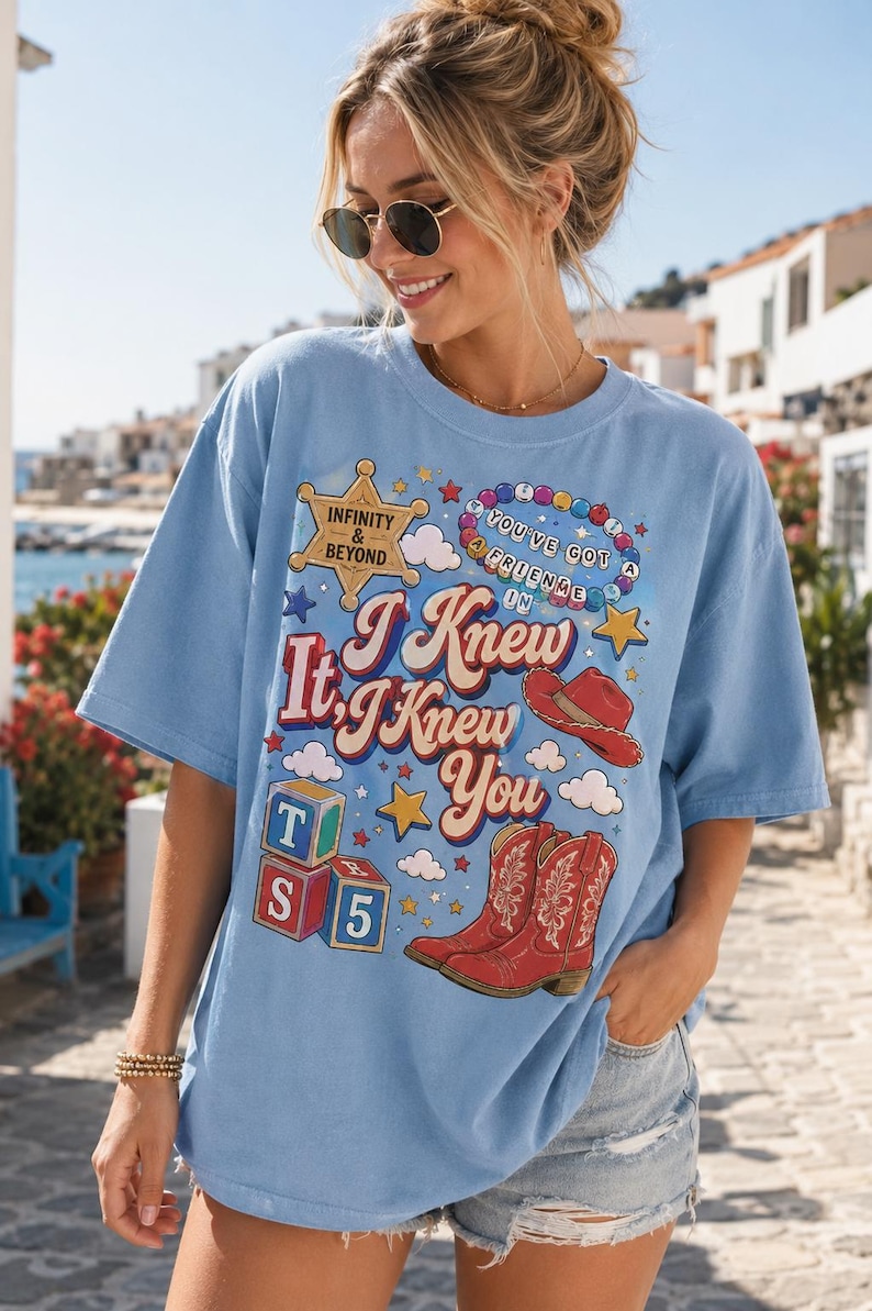 K&ouml;nnte beinhalten: Ein hellblaues T-Shirt mit kurzen &Auml;rmeln und einem Grafikdruck mit dem Text "I Knew It, I Knew You", einem Sheriffstern "Infinity & Beyond", einer Perlenkette, einem roten Cowboyhut, roten Cowboystiefeln und bunten Spielw&uuml;rfeln.