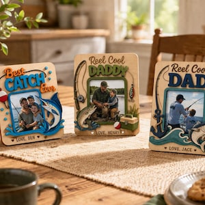 May include: Three rectangular wooden picture frames with fishing themes. The left frame says Best Catch Ever and Love, Ben. The center frame says Reel Cool Daddy and Love, Henry. The right frame says Reel Cool Dad and Love, Jace. Each features colorful cutouts of fishing gear, fish, and waves.