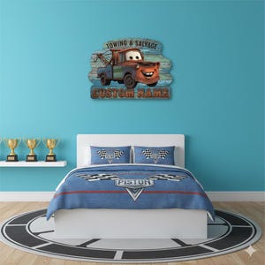 Puede incluir: Un juego de dormitorio con un tema de coche de carreras azul y rojo. La ropa de cama incluye un edred&oacute;n y dos fundas de almohada con banderas a cuadros. Encima de la cama hay un letrero de madera con un cami&oacute;n de remolque de dibujos animados y el texto "Towing & Salvage" y "Custom Name".