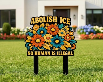 May include: A black yard sign with the text "ABOLISH ICE" and "NO HUMAN IS ILLEGAL" in yellow and white. The sign features a floral design with orange, blue, and yellow flowers.