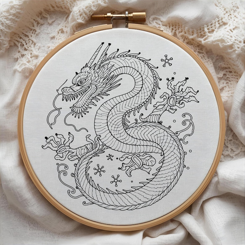 K&ouml;nnte beinhalten: Schwarz-wei&szlig; gesticktes Drachendesign auf wei&szlig;em Stoff, gespannt in einem h&ouml;lzernen Stickrahmen. Der Drache ist detailliert mit Schuppen und Krallen. Der Hintergrund ist ein weicher, wei&szlig;er Stoff. Der Rahmen hat einen Durchmesser von ca. 20 cm.