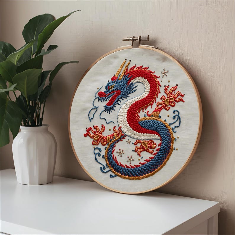K&ouml;nnte beinhalten: Gesticktes Drachenkunstwerk in einem Holzreifen. Der Drache hat rote, wei&szlig;e und blaue F&auml;den mit aufwendigen Details. Das Kunstwerk wird auf wei&szlig;em Hintergrund mit einer Pflanze in einer wei&szlig;en Vase links gezeigt.