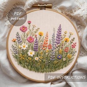 May include: Embroidered floral design in a wooden hoop. The artwork features a vibrant array of colorful flowers, including pink, yellow, purple, and orange blooms, set against a cream-colored fabric. The text "PDF pattern" and "PDF instructions" are visible.