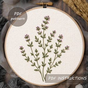 Puede incluir: Diseño floral bordado en un aro de madera. El bordado presenta tallos y hojas verdes con pequeños racimos de flores moradas. El texto "PDF pattern" y "PDF instructions" es visible. El fondo es de tela neutra.