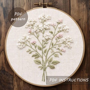 May include: An embroidery hoop with a floral design. The design features white and pink flowers with green leaves, stitched on a cream-colored fabric. The text "PDF pattern" and "PDF instructions" are visible.