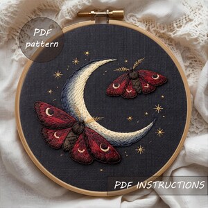 Könnte beinhalten: Gesticktes Wandbild mit einem Halbmond und zwei Motten mit rot-braunen Flügeln. Der Mond ist in Blau-, Creme- und Goldtönen gestickt. Dunkelgrauer Hintergrund mit goldenen Sternen. Text: "PDF pattern" und "PDF instructions".