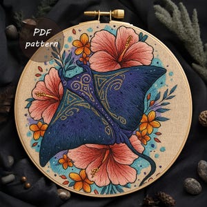 May include: A detailed embroidery hoop featuring a blue manta ray design with gold accents, surrounded by pink and orange hibiscus flowers and foliage. The text "PDF pattern" is visible. The artwork is set against a neutral fabric background.