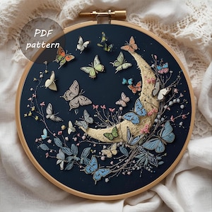 Puede incluir: Un bastidor de bordado artesanal con un fondo azul oscuro, una luna creciente y numerosas mariposas coloridas. El diseño incluye el texto "PDF pattern" en un marco circular, con un aro de madera.
