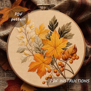 Peut inclure: Un tambour à broder contenant un panneau en tissu beige avec un motif brodé de feuilles d'automne et de baies. Le design présente des feuilles d'érable jaunes, orange et vertes ainsi que de petites baies rondes sur des tiges brunes. Texte PDF pattern.
