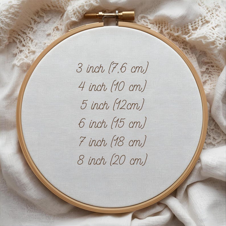 May include: A wooden embroidery hoop with a white fabric center. The text on the fabric indicates sizes: 3 inch (7.6 cm), 4 inch (10 cm), 5 inch (12cm), 6 inch (15 cm), 7 inch (18 cm), and 8 inch (20 cm).