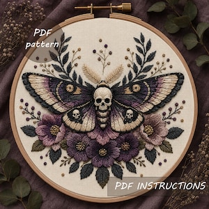 May include: An embroidery hoop containing a fabric piece with a moth design featuring a skull head and two smaller skulls on the wings. The moth is surrounded by purple flowers, dark green leaves, and thin stems. Text reads PDF pattern and PDF INSTRUCTIONS.