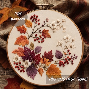 May include: An embroidery hoop containing a fabric panel with a stitched design of autumn leaves, red berries, and white flowers. The text PDF pattern and PDF INSTRUCTIONS are visible on the image. The design features orange, red, and purple foliage.