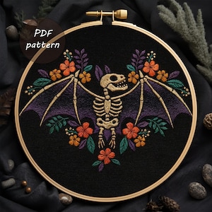 May include: An embroidered hoop art piece featuring a bat skeleton with purple wings, surrounded by orange and green floral accents, set against a black fabric background. The text "PDF pattern" is in the upper left corner. The embroidery is in a wooden hoop.