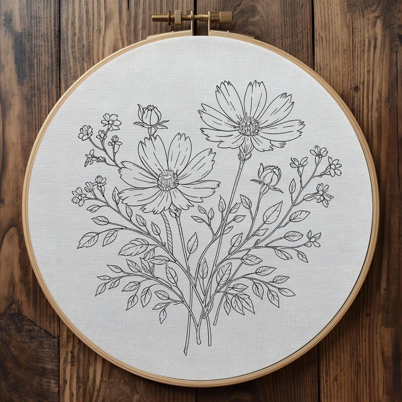 Puede incluir: Un bastidor de bordado floral con un detallado dibujo lineal en blanco y negro de flores de cosmos, capullos y follaje. El dise&ntilde;o est&aacute; centrado en una tela blanca, dentro de un bastidor de madera redondo con cierre de lat&oacute;n.