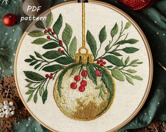 Könnte beinhalten: Gesticktes Weihnachtsornament-Design in einem Holzreifen. Das Ornament ist goldfarben mit grünen Blättern und roten Beeren. Der Text "PDF pattern" befindet sich in einem Kreis oben links. Der Hintergrund ist ein dunkelgrüner Stoff.