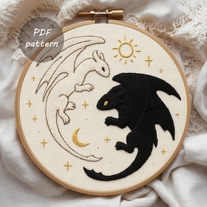 Könnte beinhalten: Gestickte Drachenkunst in einem Holzreifen. Ein weißer Drache und ein schwarzer Drache blicken sich an, mit einer goldenen Sonne und einem Mond. Goldene Kreuz- und Sternakzente umgeben die Drachen. Der Text "PDF pattern" befindet sich in einem Kreis oben.
