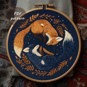 May include: Embroidered hoop art showing two foxes, one orange and one blue, against a dark blue backdrop with stars. The foxes are encircled by brown leaves. The text "PDF pattern" is visible.