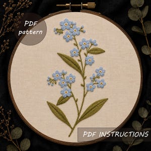 Puede incluir: Un bastidor de bordado circular de madera que contiene un panel de tela beige con flores nomeolvides azul claro y hojas verdes bordadas a mano. El texto PDF pattern y PDF INSTRUCTIONS es visible en la tela.