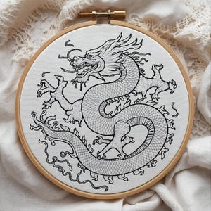 May include: A black and white embroidered dragon design on white fabric, stretched within a wooden embroidery hoop. The dragon is detailed with scales and flowing lines, set against a neutral background.