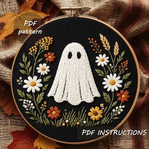 Pode incluir: Bordado num bastidor de madeira, com um fantasma branco de olhos pretos, rodeado por flores coloridas e vegetação sobre fundo preto. O texto "PDF pattern" e "PDF instructions" é visível.