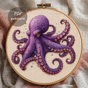 Könnte beinhalten: Detaillierte Stickerei eines lila Oktopus mit rosa Saugnäpfen, in einem hölzernen Stickrahmen. Der Oktopus ist der Mittelpunkt, mit seinen Tentakeln, die sich um den Rahmen winden. Der Text "PDF pattern" befindet sich in einem Kreis oben links.
