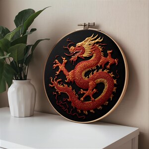 May include: Embroidered dragon art in a wooden hoop. The dragon is red and gold against a black background. The embroidery is detailed, showing the dragon's scales and features. The hoop is displayed on a white surface.