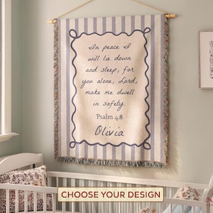 May include: A beige and blue striped wall tapestry with the text "In peace I will lie down and sleep, for you alone, Lord, make me dwell in safety. Psalm 4:8 Olivia." The tapestry is hanging above a white crib.