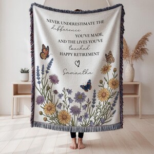 May include: A woven throw blanket featuring a cream background with a floral and butterfly print. The text reads: NEVER UNDERESTIMATE THE difference YOU'VE MADE, AND THE LIVES YOU'VE touched HAPPY RETIREMENT, with the name Samantha and a heart.