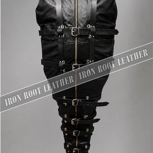 Op de afbeelding: Een zwarte lederen dwangzak met een centrale goudkleurige rits, een hoge kraag met metalen studs en meerdere verstelbare lederen riemen met goudkleurige gespen. De tekst IRON ROOT LEATHER is diagonaal over het midden gedrukt.