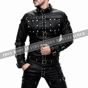 May include: A black leather jacket and matching pants set featuring silver-toned metal studs, multiple adjustable buckled straps across the chest, arms, and legs, and lace-up detailing. The text IRON ROOT LEATHER is printed across the center.