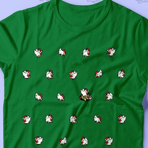 Puede incluir: Una camiseta verde con un patrón repetido de pollos blancos. Un personaje pixelado con una gorra roja y sosteniendo una espada está en el centro de la camiseta.