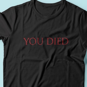 Może przedstawiać: Czarny T-shirt z napisem "YOU DIED" w czerwonych literach.