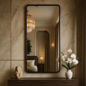 以下が含まれることがあります： 黒いフレームの大きな長方形の鏡が置かれた、6つの引き出しと真鍮の取っ手が付いた濃い茶色のドレッサー。白い花が入った白い花瓶と装飾用の石がドレッサーの上に置かれています。鏡は寝室を映しています。