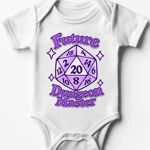 Könnte beinhalten: Ein weißer kurzärmeliger Babybody mit einer violetten Grafik eines zwanzigseitigen Würfels und dem Text Future Dungeon Master. Der Würfel zeigt die Zahlen 2, 4, 6, 8, 10, 12, 14, 16, 18 und 20 und ist von vier kleinen violetten Sternen umgeben.